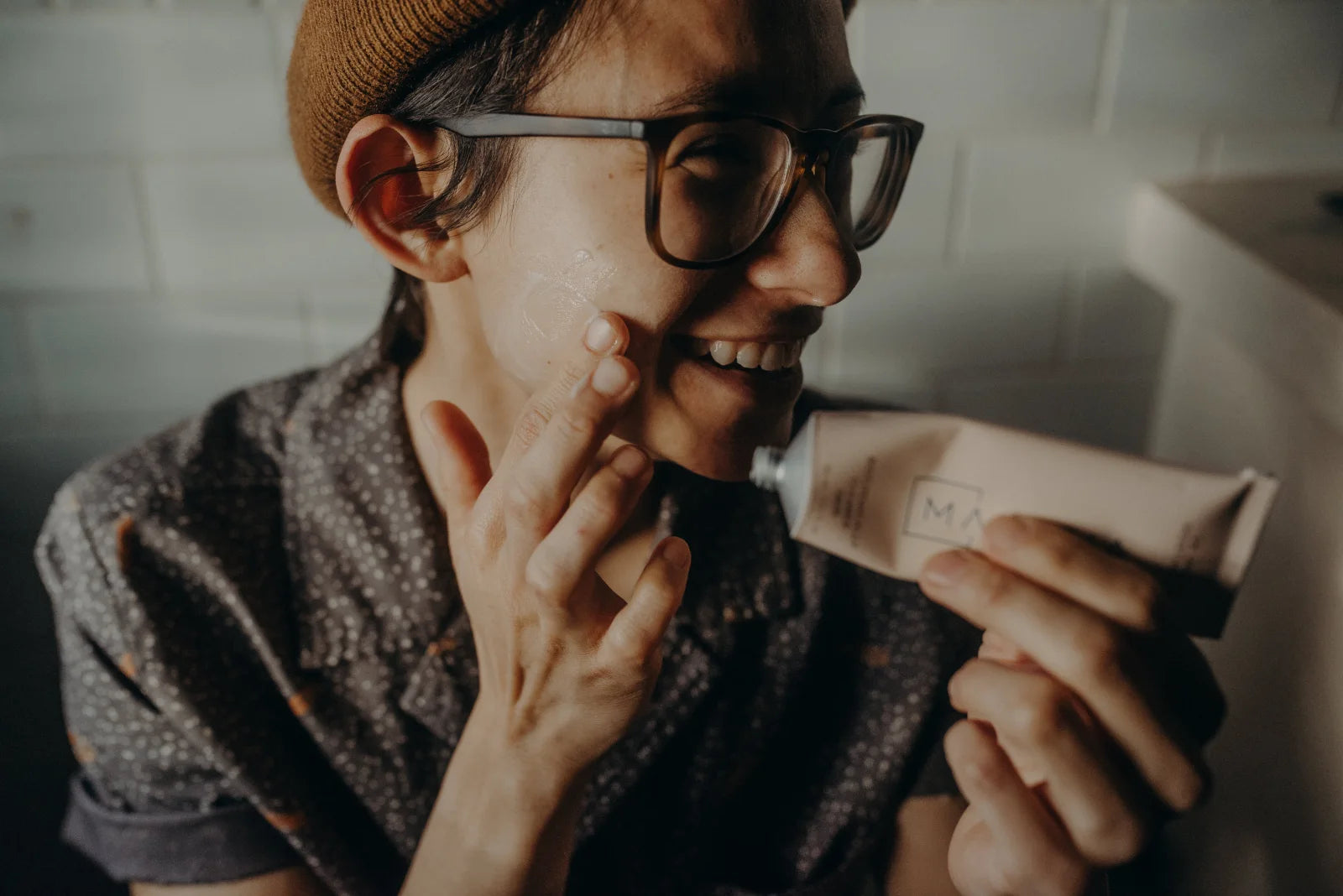 A friend of Malezia smiling while applying moisturizer, Malezia tube in hand